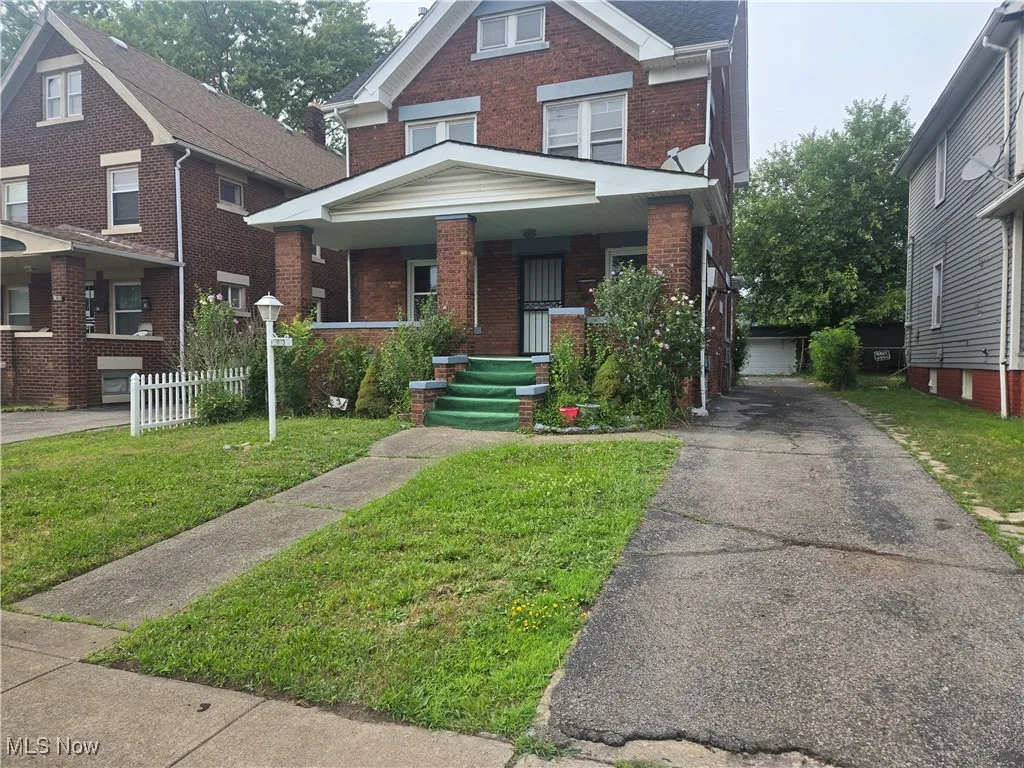 View of front facade featuring brick siding, covered porch, an outdoor structure, and a front lawn
