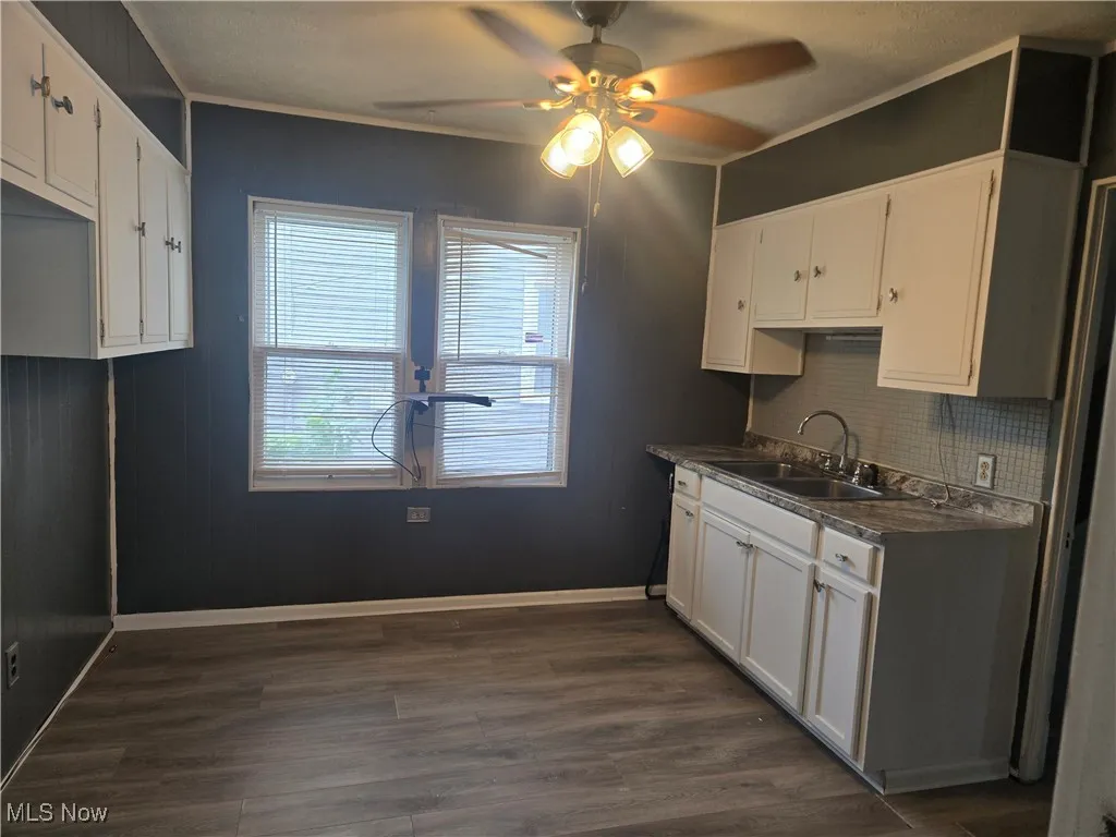 Kitchen with a ceiling fan, dark wood-style flooring, white cabinetry, crown molding, and dark countertops