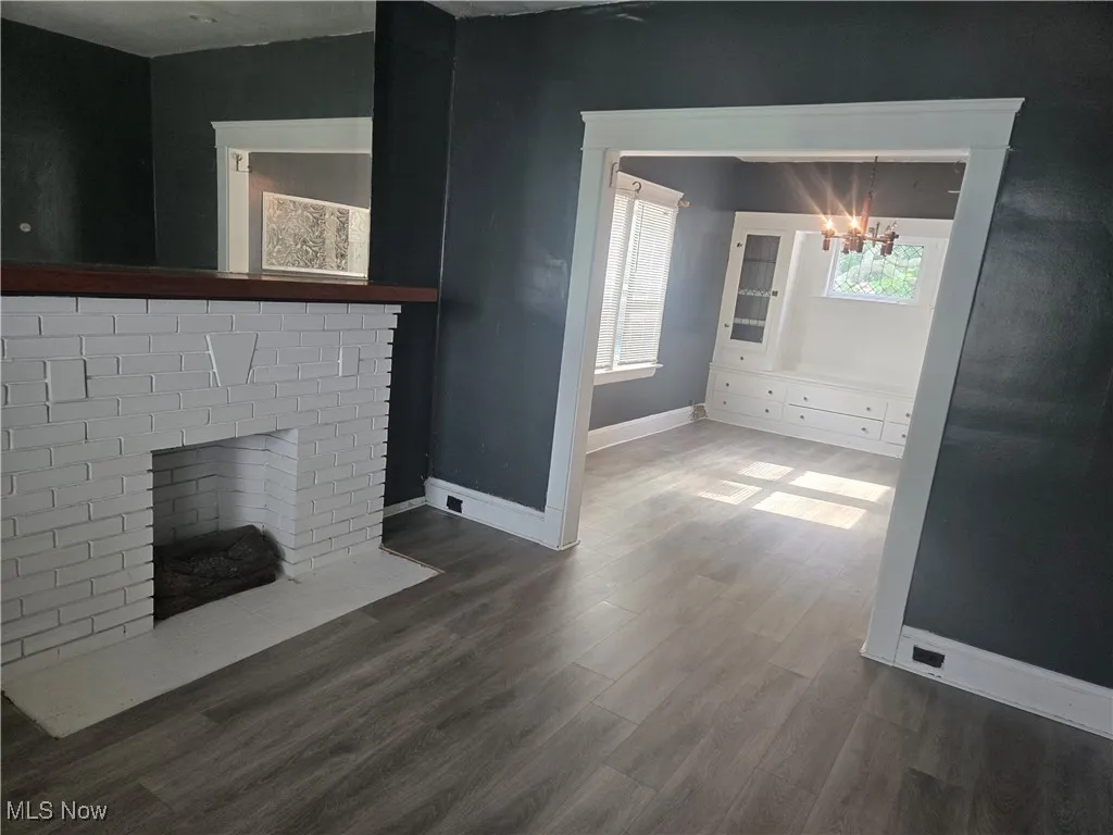 Unfurnished living room featuring dark wood-type flooring, a brick fireplace, and a chandelier