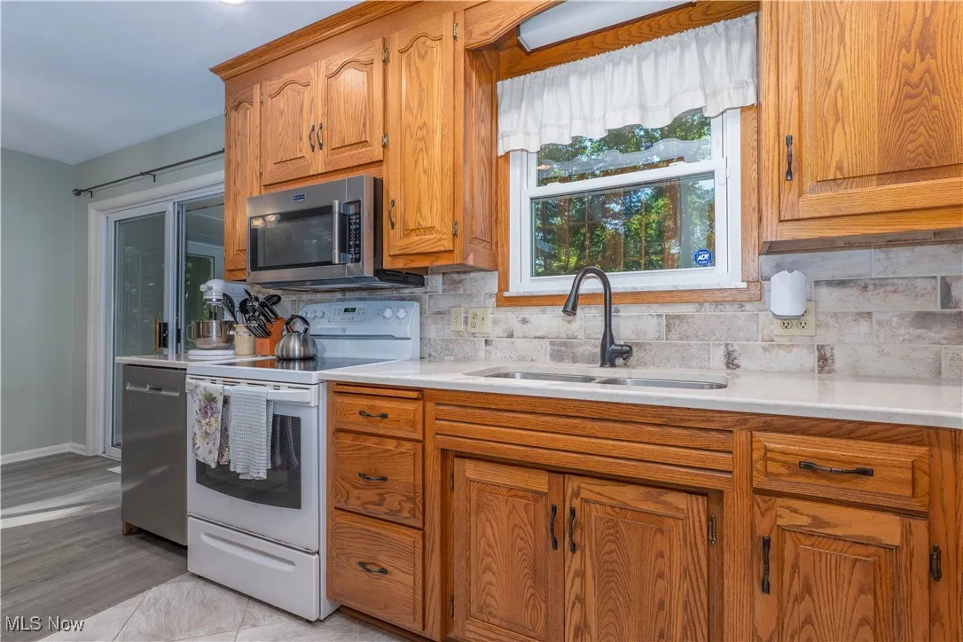 Kitchen featuring stainless steel appliances, tasteful backsplash, brown cabinets, light stone countertops, and light tile patterned floors