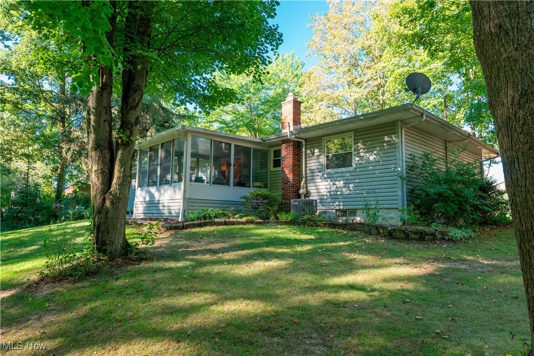 View of vback of home featuring a sunroom, a chimney, and the back lawn