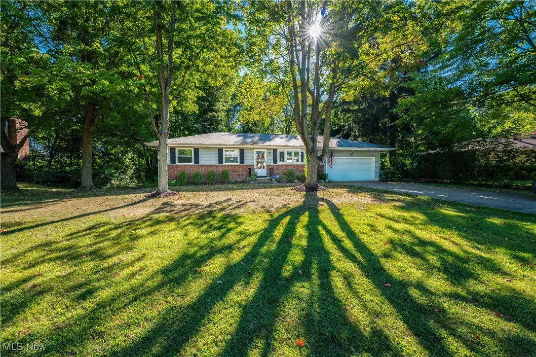 Ranch-style house with a garage, a front lawn, driveway, and view of wooded area