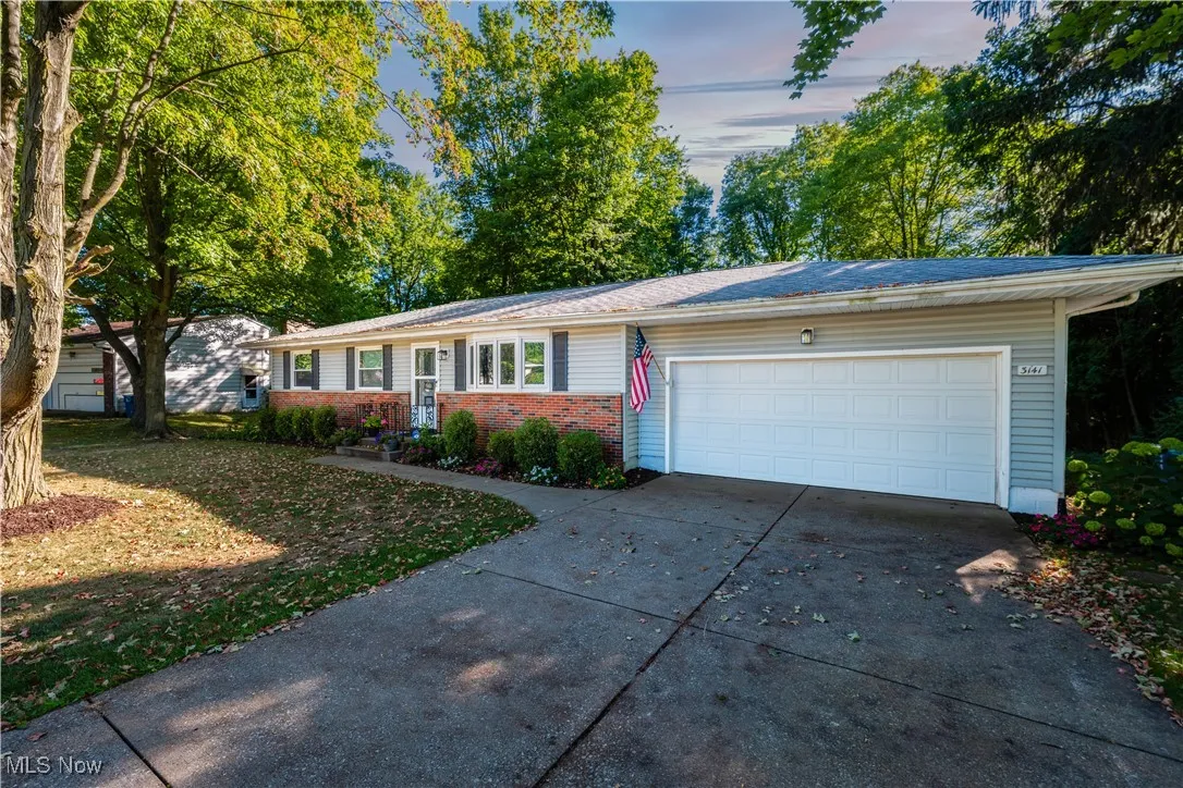 Single story home with an attached garage, driveway, brick siding, and a lawn