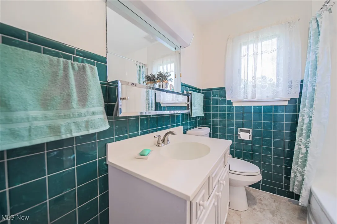 Full bathroom featuring tile walls, vanity, tile patterned floors, a wainscoted wall, and shower / bathtub combination with curtain