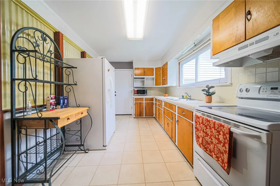 Kitchen featuring white appliances, light countertops, brown cabinets, light tile patterned flooring, and tasteful backsplash