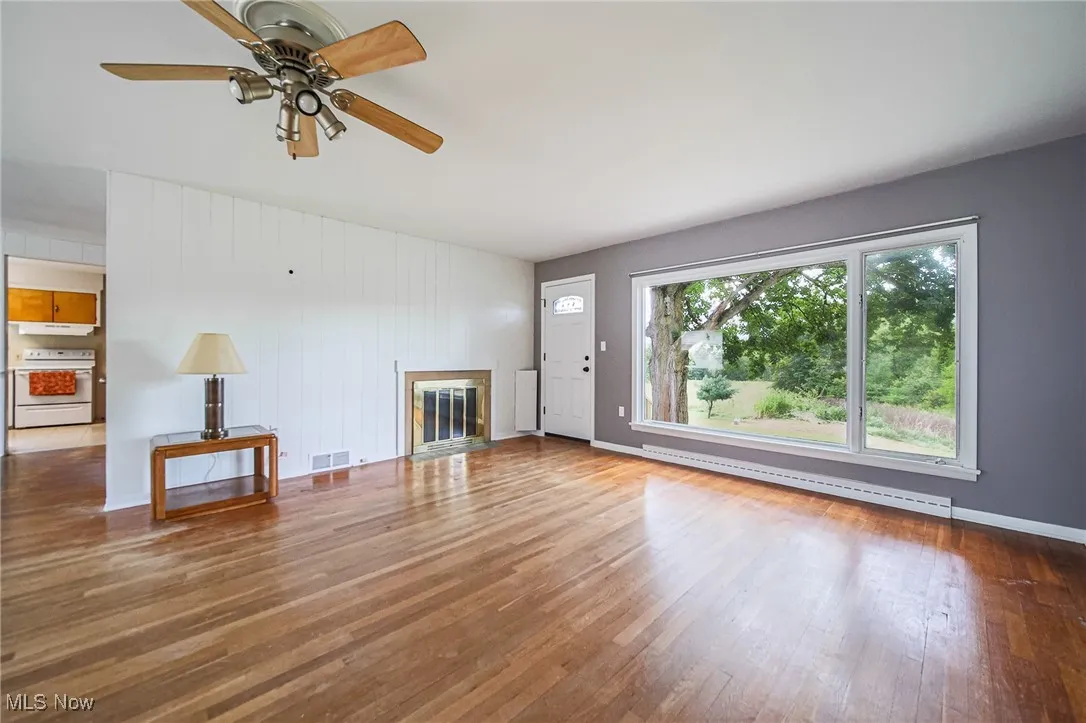 Unfurnished living room with wood-type flooring, a ceiling fan, and a glass covered fireplace
