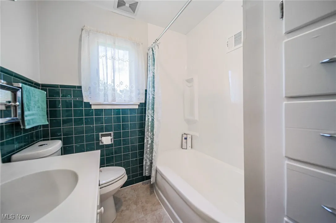 Full bathroom with tile walls, shower / bath combo with shower curtain, vanity, wainscoting, and light tile patterned flooring