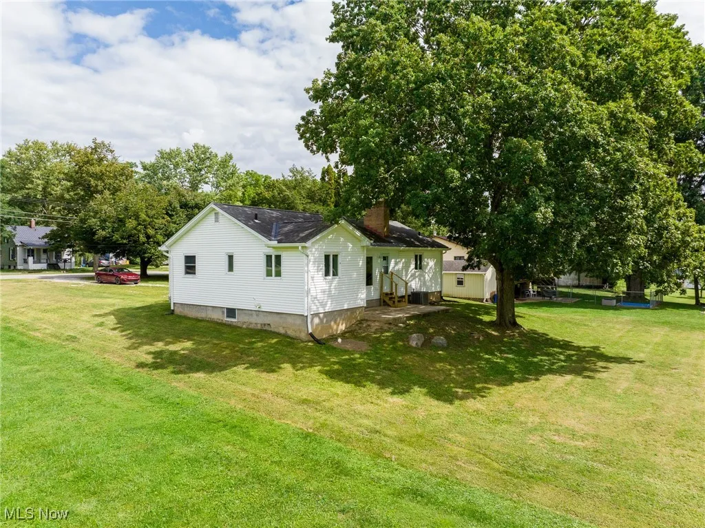 View of side of property featuring a lawn, a chimney, and view of wooded area