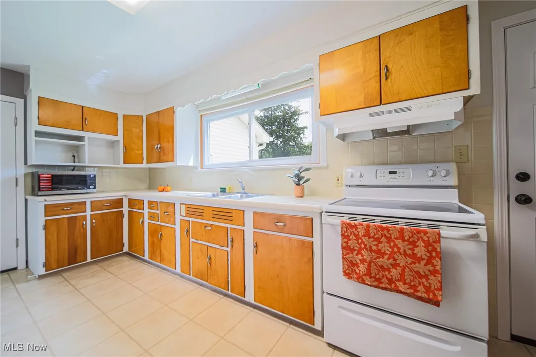 Kitchen with white range with electric cooktop, tasteful backsplash, light countertops, under cabinet range hood, and open shelves