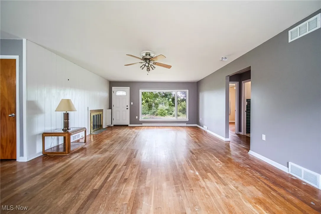 Unfurnished living room with wood-type flooring, a ceiling fan, and a glass covered fireplace