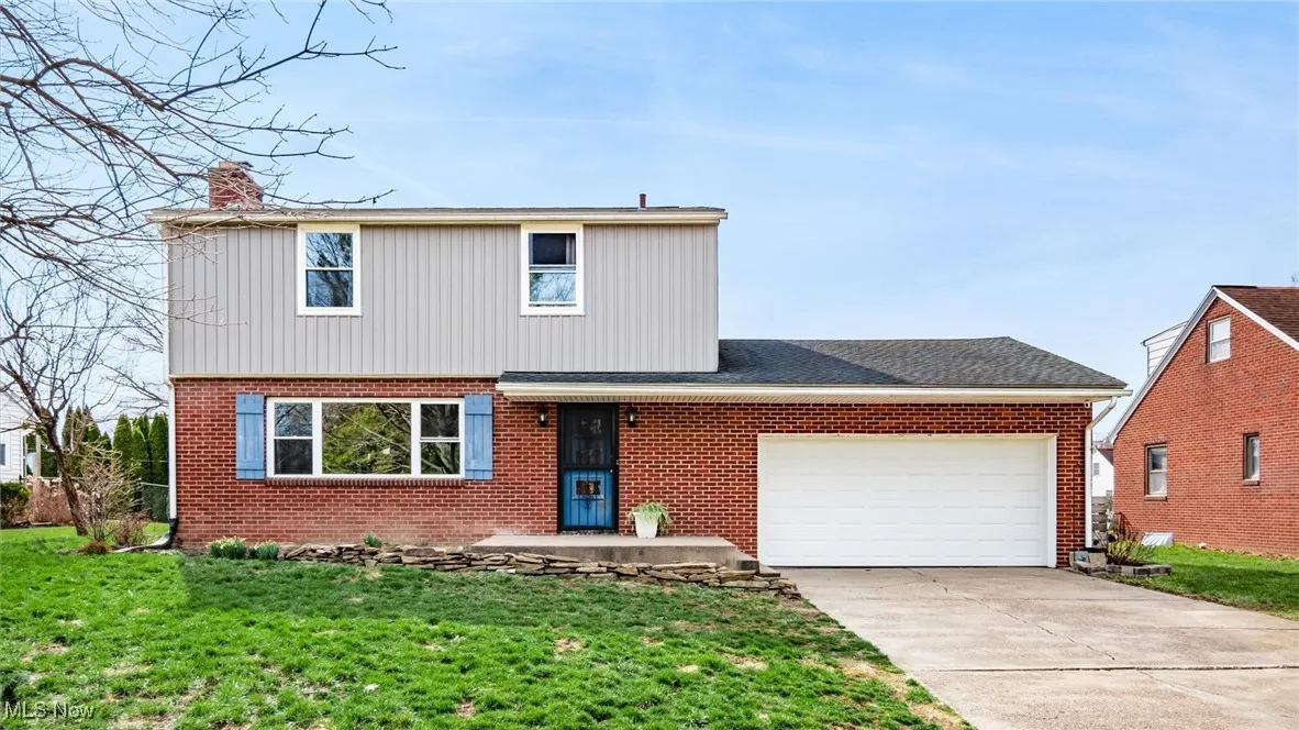 View of front of house with an attached garage, concrete driveway, brick siding, a front yard, and a chimney