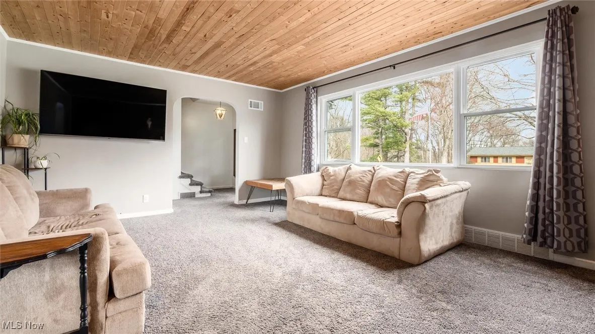 Carpeted living room featuring arched walkways, stairs, wooden ceiling, and ornamental molding