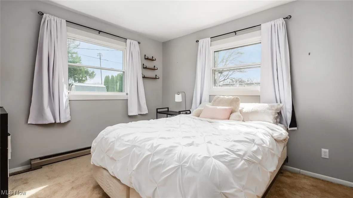 Bedroom with a baseboard heating unit and light carpet
