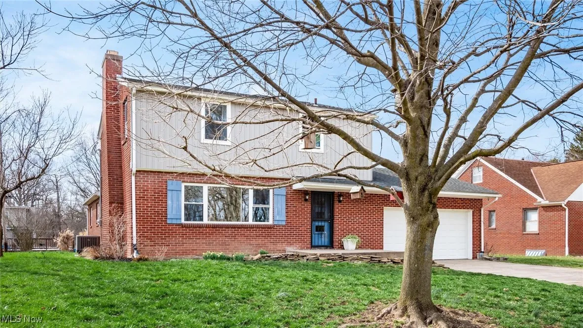 View of front of house featuring a chimney, driveway, an attached garage, and brick siding