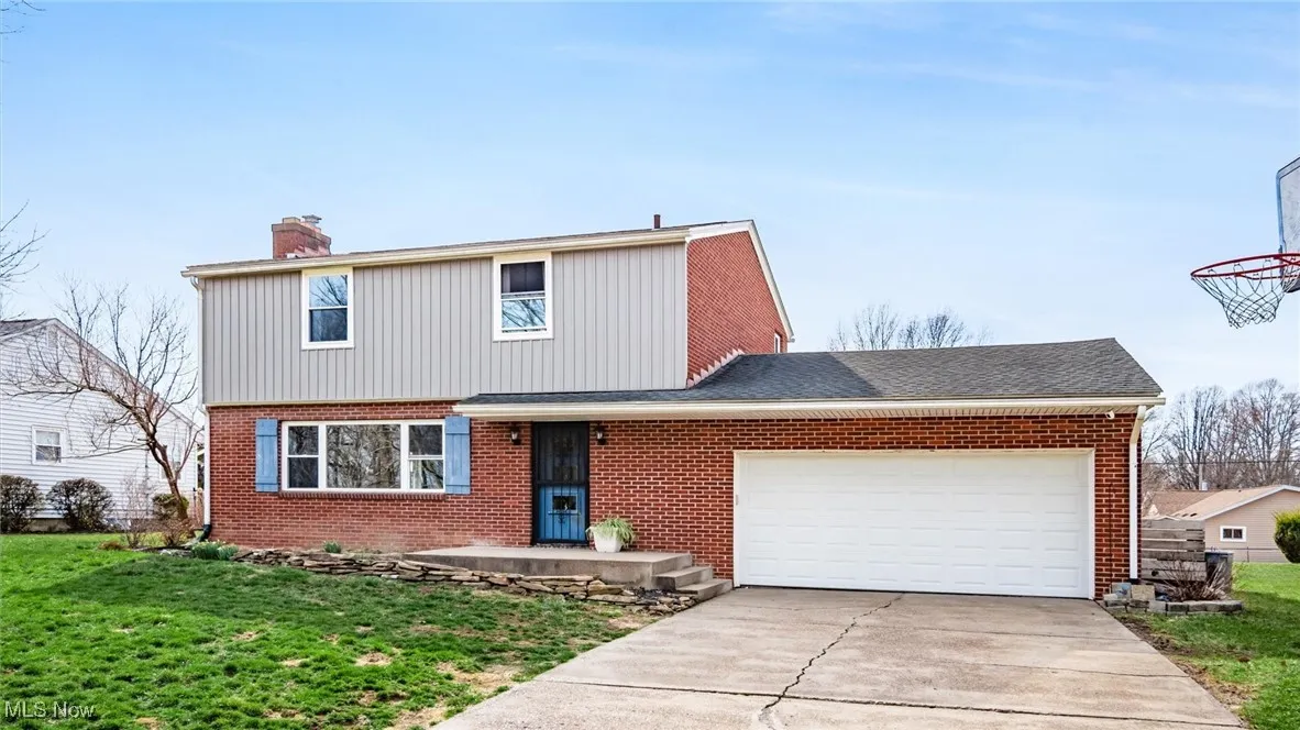 View of front facade featuring a garage, brick siding, a front lawn, concrete driveway, and a chimney