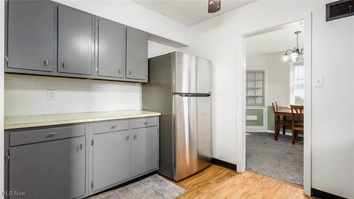 Kitchen featuring gray cabinets, freestanding refrigerator, light wood-style flooring, light countertops, and a chandelier