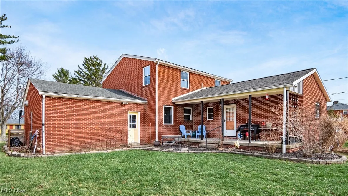 Back of house with a yard, brick siding, roof with shingles, and a deck