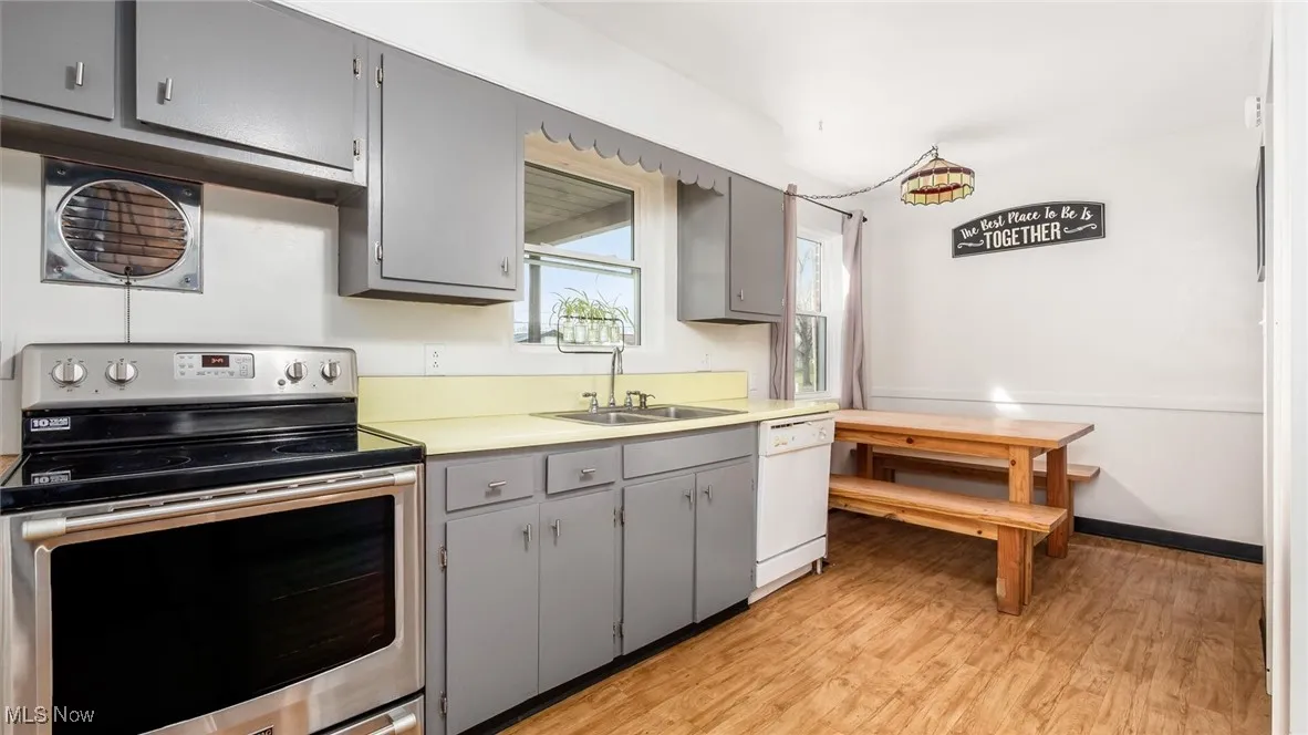 Kitchen with gray cabinets, stainless steel electric range oven, light wood-style floors, light countertops, and dishwasher