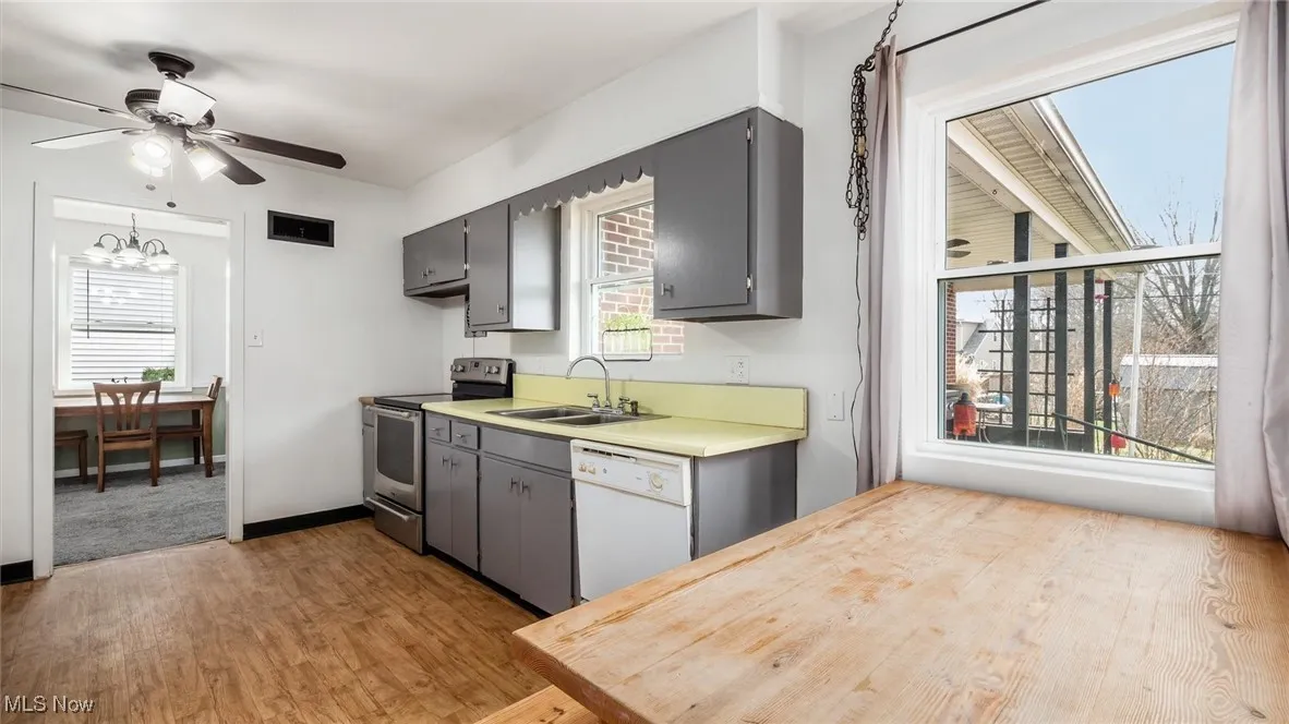 Kitchen with stainless steel electric stove, light wood-type flooring, light countertops, white dishwasher, and a ceiling fan