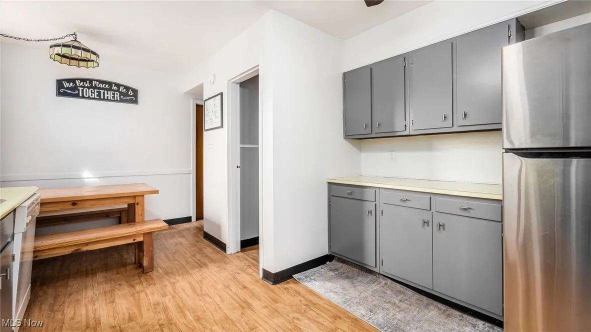 Kitchen with gray cabinetry, freestanding refrigerator, light countertops, and light wood-style flooring