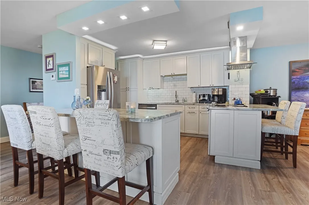 Kitchen featuring a breakfast bar, stainless steel fridge with ice dispenser, dark wood-style flooring, and light stone counters