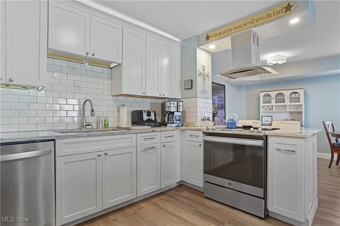 remodeled Kitchen with newer appliances with stainless steel finishes, light stone counters, white cabinets, and subway tile backsplash