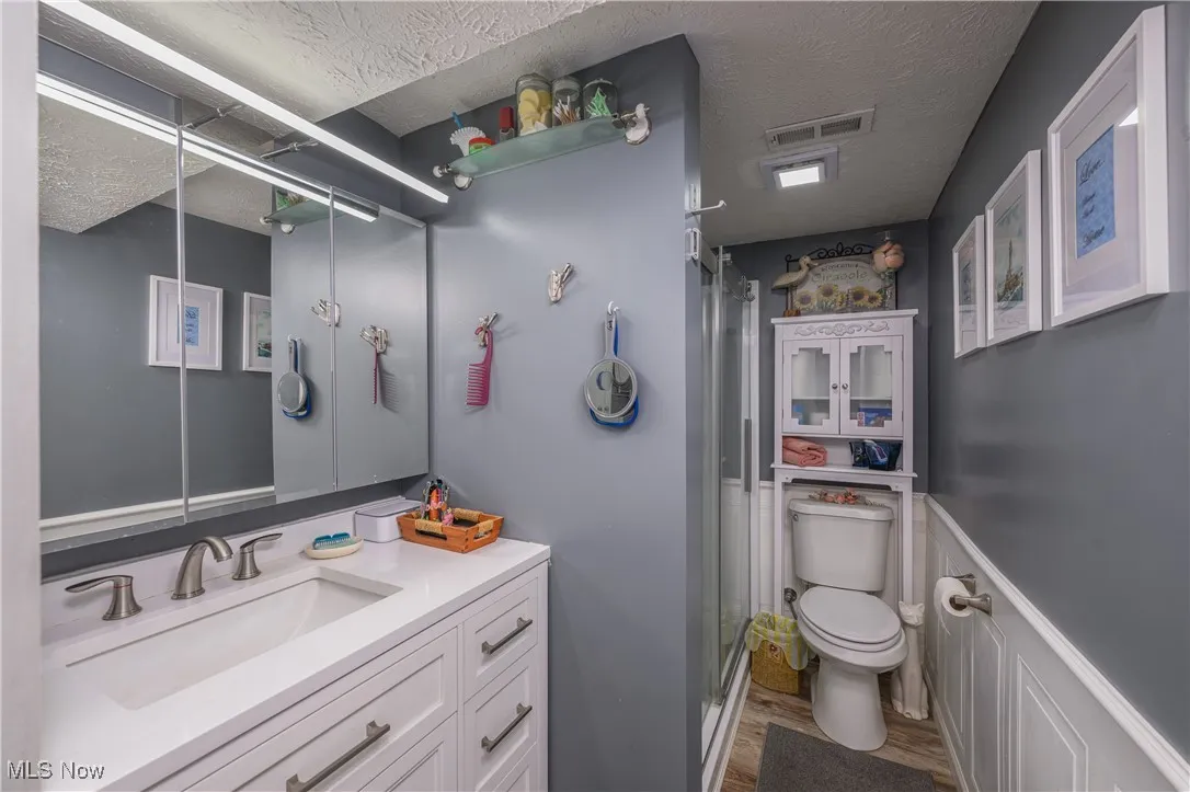 Bathroom with a stall shower, vanity, wood finished floors, a textured ceiling, and a wainscoted wall