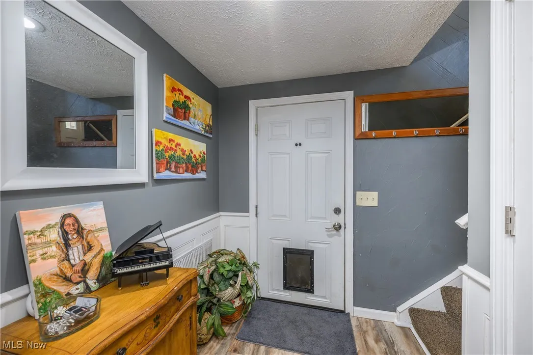Doorway with a textured ceiling, wood finished floors, stairs, and wainscoting