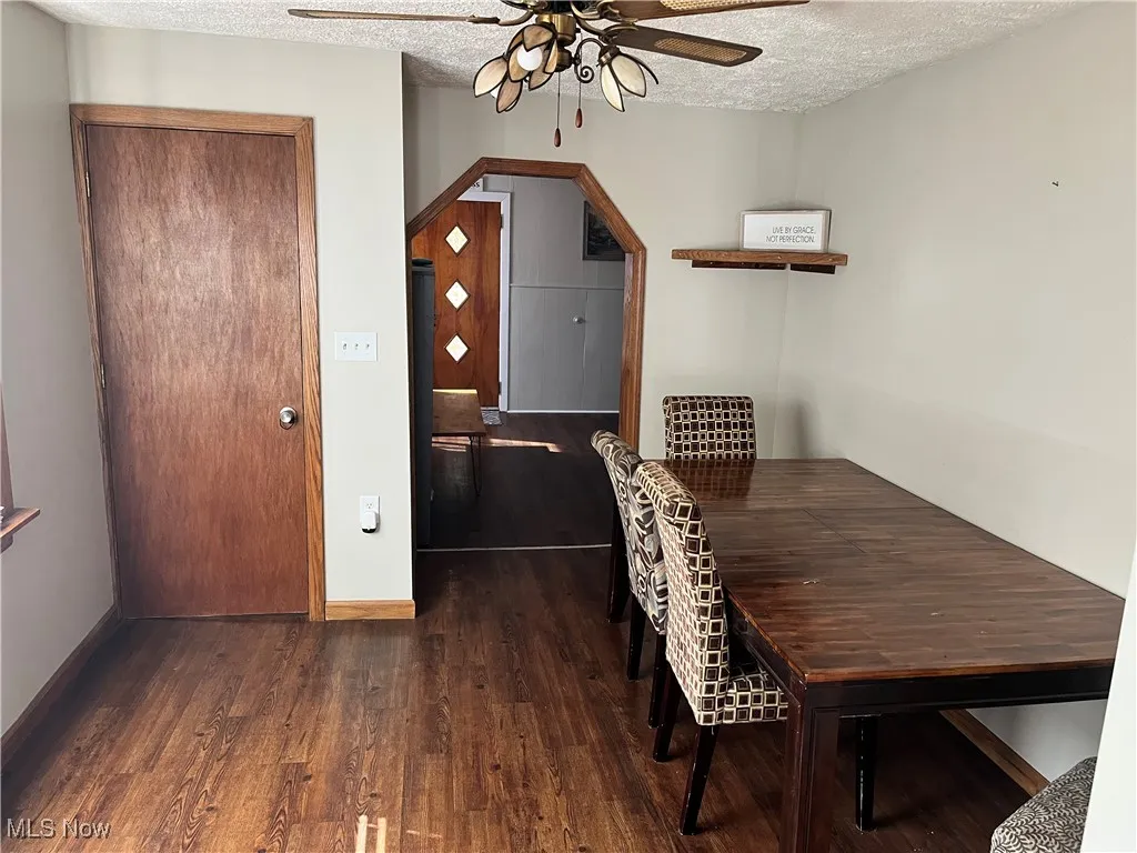 Dining room featuring a textured ceiling, dark wood-type flooring, ceiling fan, and arched walkways