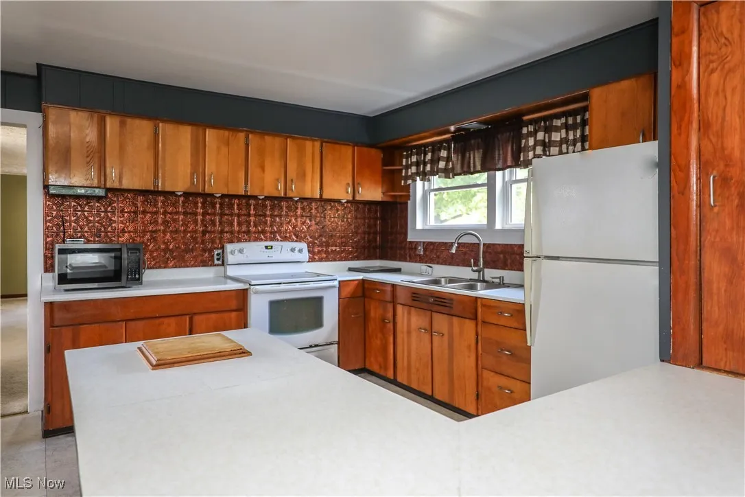 Kitchen with white appliances, light countertops, brown cabinets, and open shelves