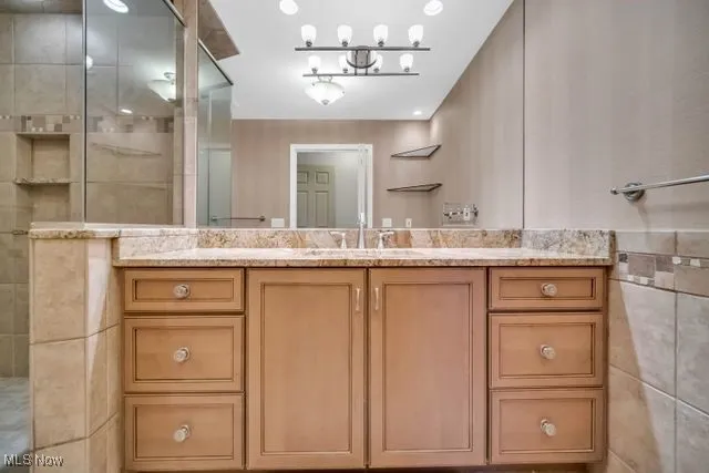 Bathroom with tile walls, a shower, and vanity