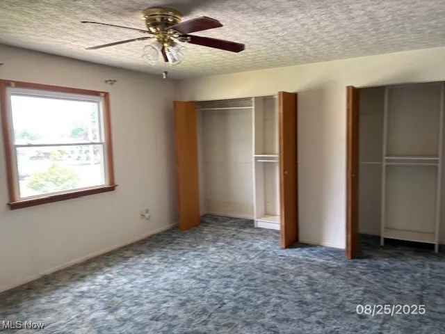 Unfurnished bedroom with two closets, carpet flooring, a textured ceiling, and ceiling fan