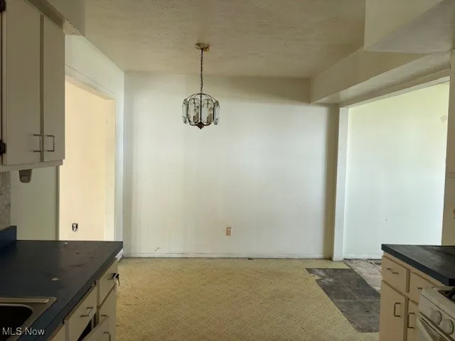 Unfurnished dining area featuring light carpet, a chandelier, and a textured ceiling