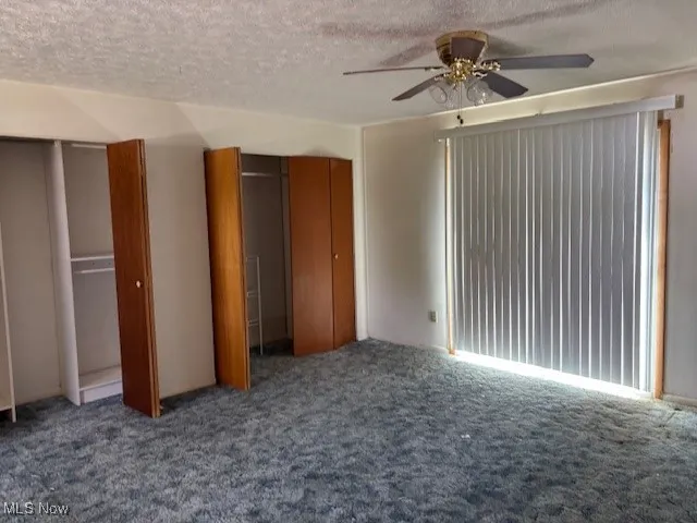 Unfurnished bedroom featuring multiple closets, a textured ceiling, carpet, and ceiling fan