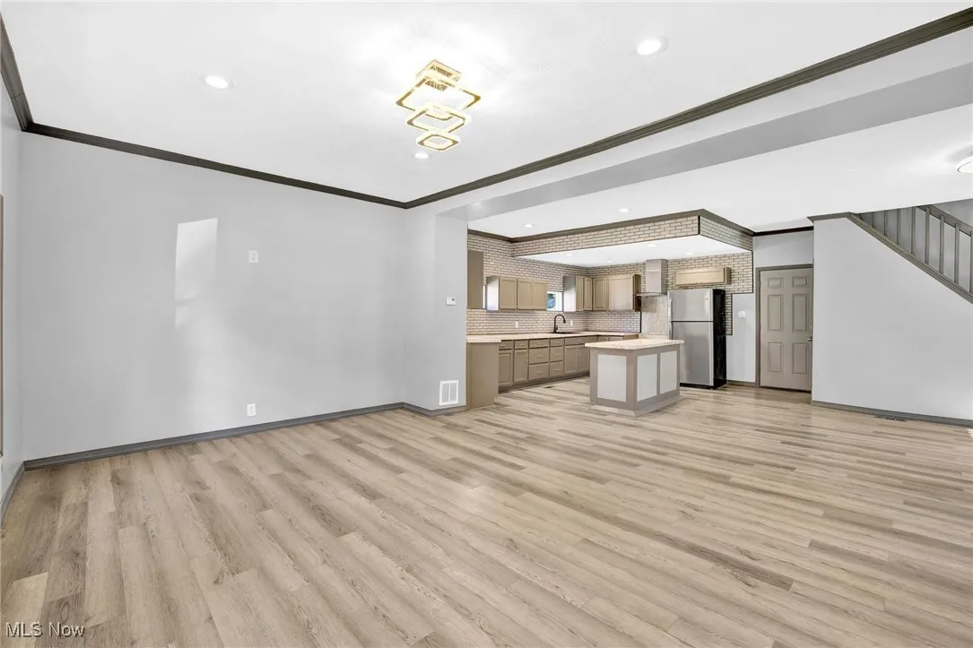 Kitchen with open floor plan, crown molding, light countertops, freestanding refrigerator, and light wood finished floors