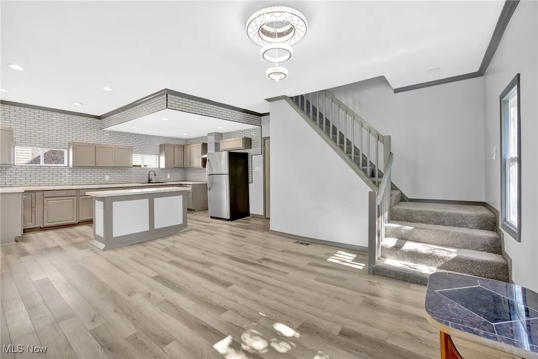 Kitchen featuring gray cabinets, crown molding, freestanding refrigerator, decorative backsplash, and light wood finished floors
