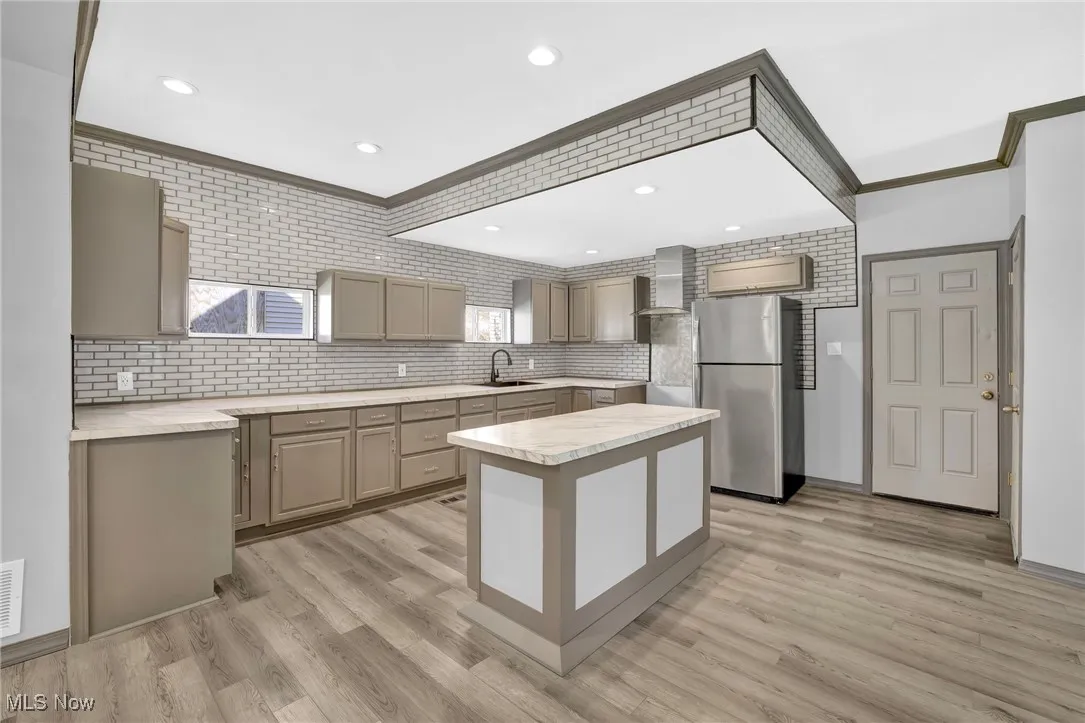 Kitchen featuring gray cabinetry, freestanding refrigerator, light countertops, tasteful backsplash, and crown molding