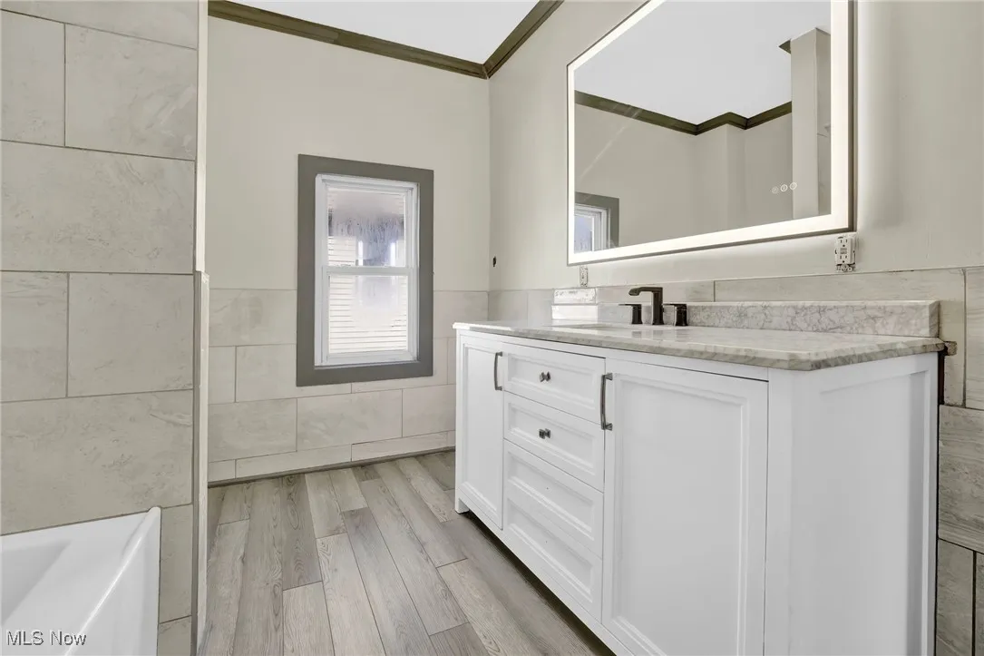 Bathroom featuring tile walls, vanity, wainscoting, a tub, and light wood-style flooring
