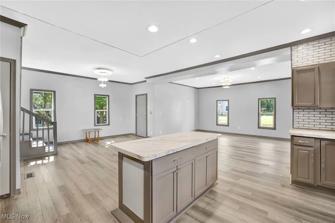 Kitchen with open floor plan, light countertops, light wood finished floors, ornamental molding, and decorative backsplash