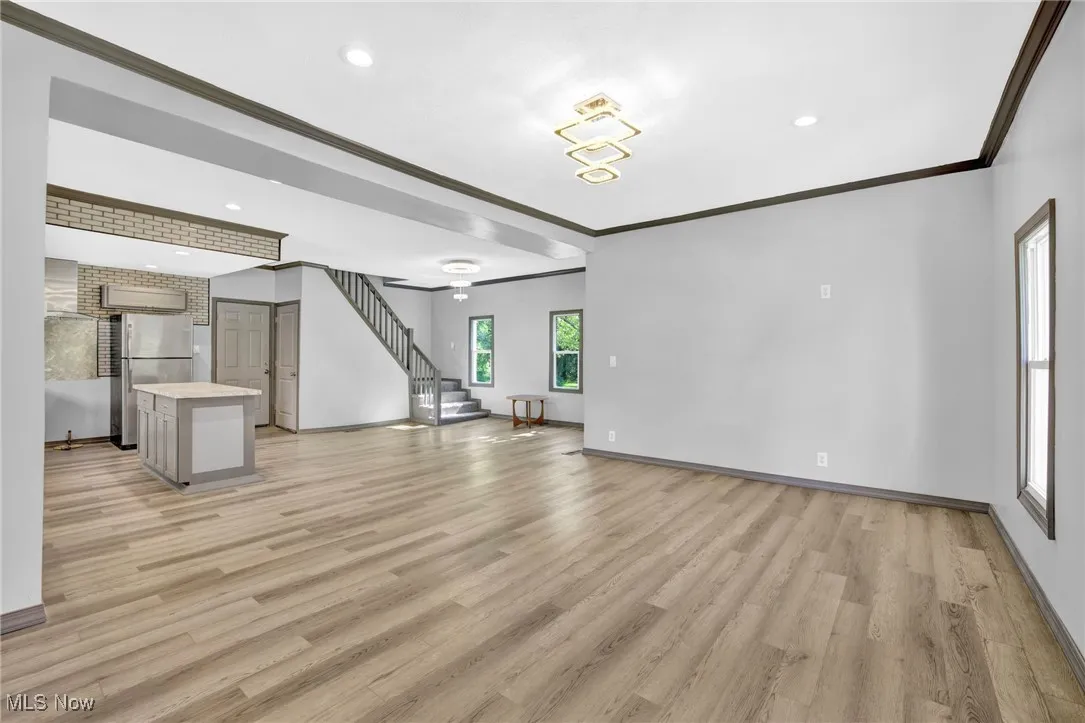 Unfurnished living room with ornamental molding, light wood finished floors, stairway, and recessed lighting