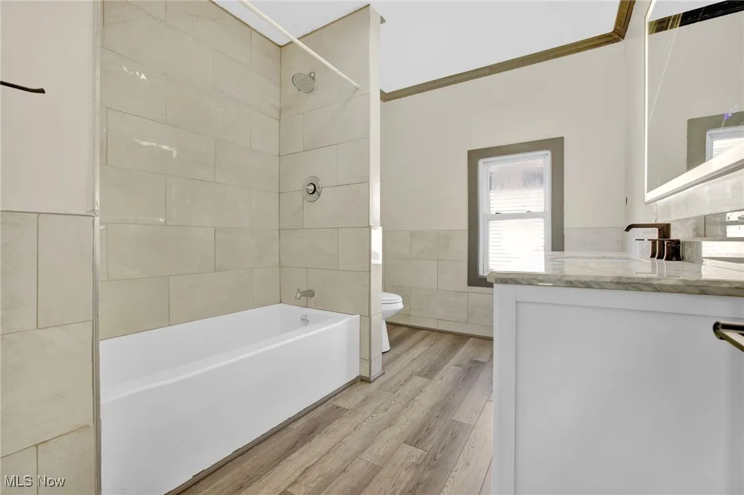 Bathroom featuring washtub / shower combination, vanity, tile walls, light wood-style flooring, and crown molding