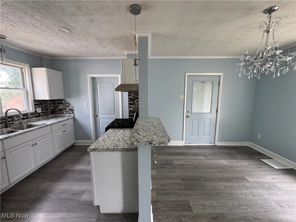Kitchen featuring white cabinets, pendant lighting, a chandelier, ornamental molding, and light stone countertops
