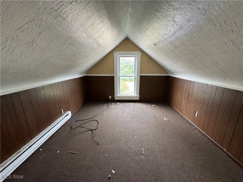 Bonus Room 1 with wooden walls, a baseboard heating unit, a textured ceiling, carpet flooring, and vaulted ceiling