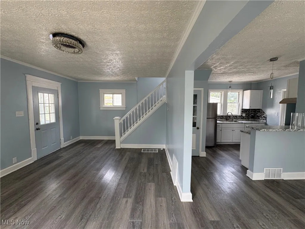 Foyer entrance with ornamental molding, a textured ceiling, dark wood-style floors, and stairs