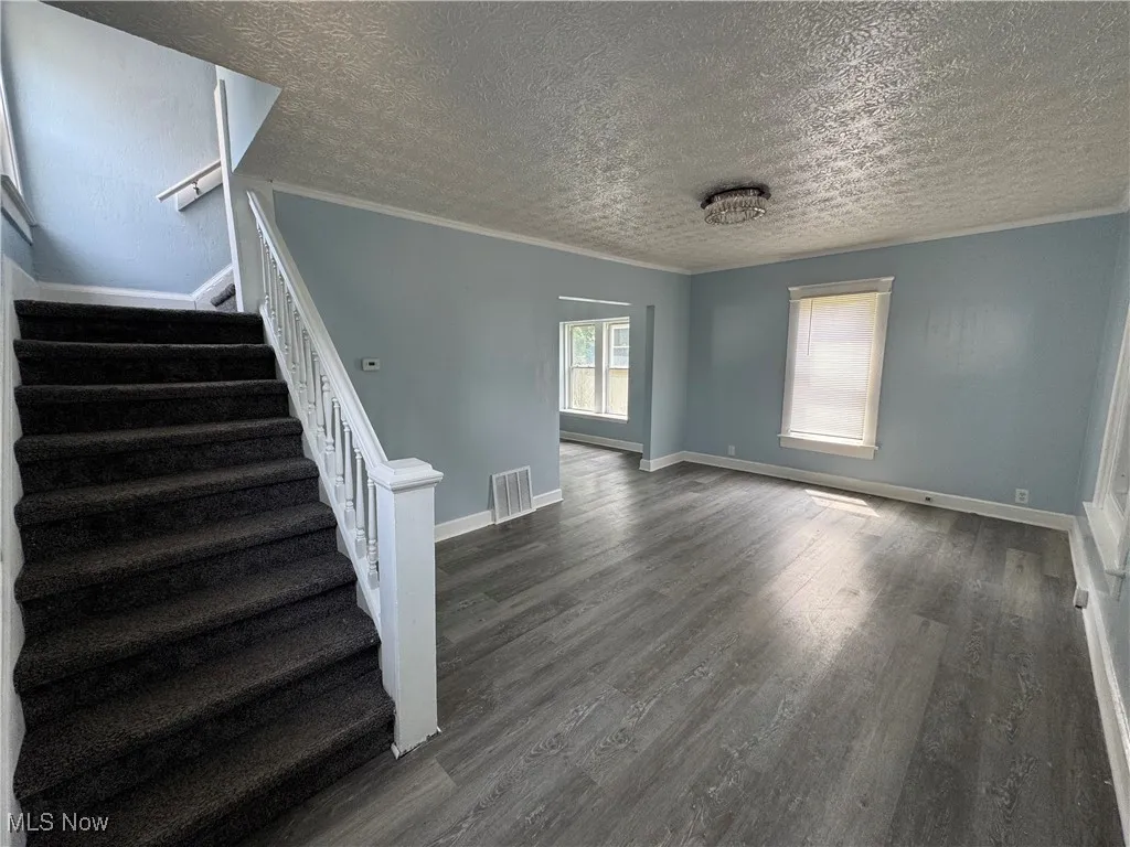 Unfurnished living room featuring crown molding, dark wood finished floors, stairs, and a textured ceiling