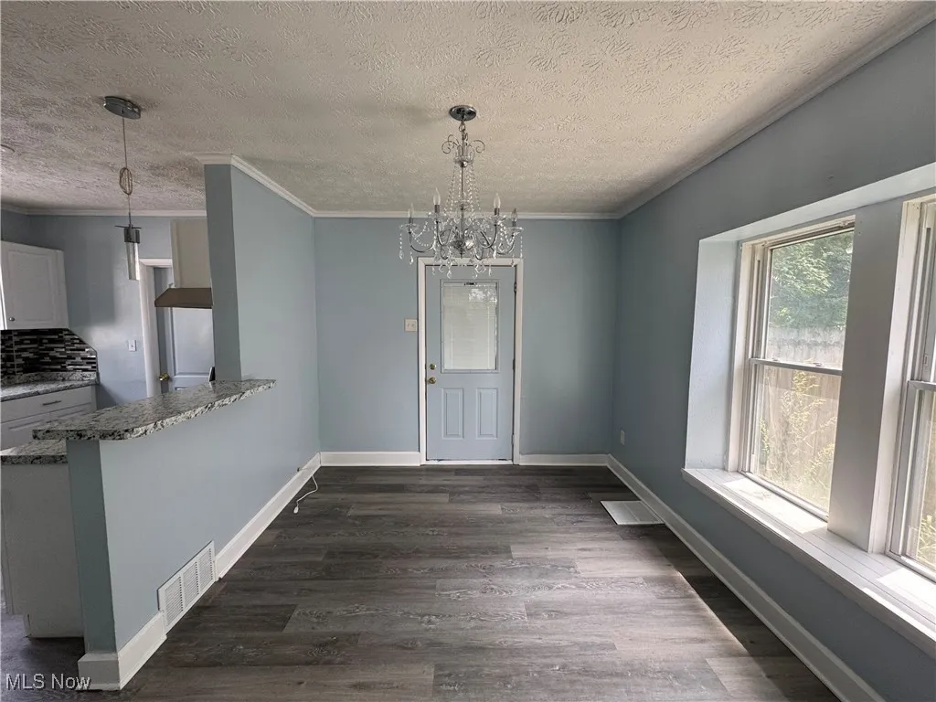 Unfurnished dining area featuring crown molding, a chandelier, a textured ceiling, and dark wood finished floors