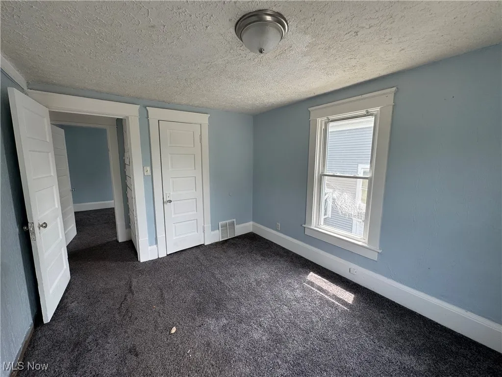 Bedroom 2 with dark colored carpet, a textured ceiling, and a closet