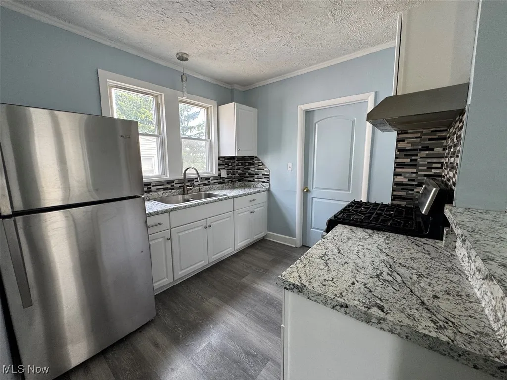 Kitchen featuring freestanding refrigerator, crown molding, white cabinets, backsplash, and wall chimney range hood
