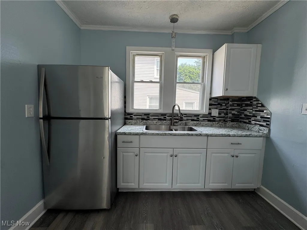 Kitchen with freestanding refrigerator, white cabinets, dark wood-style flooring, crown molding, and a textured ceiling