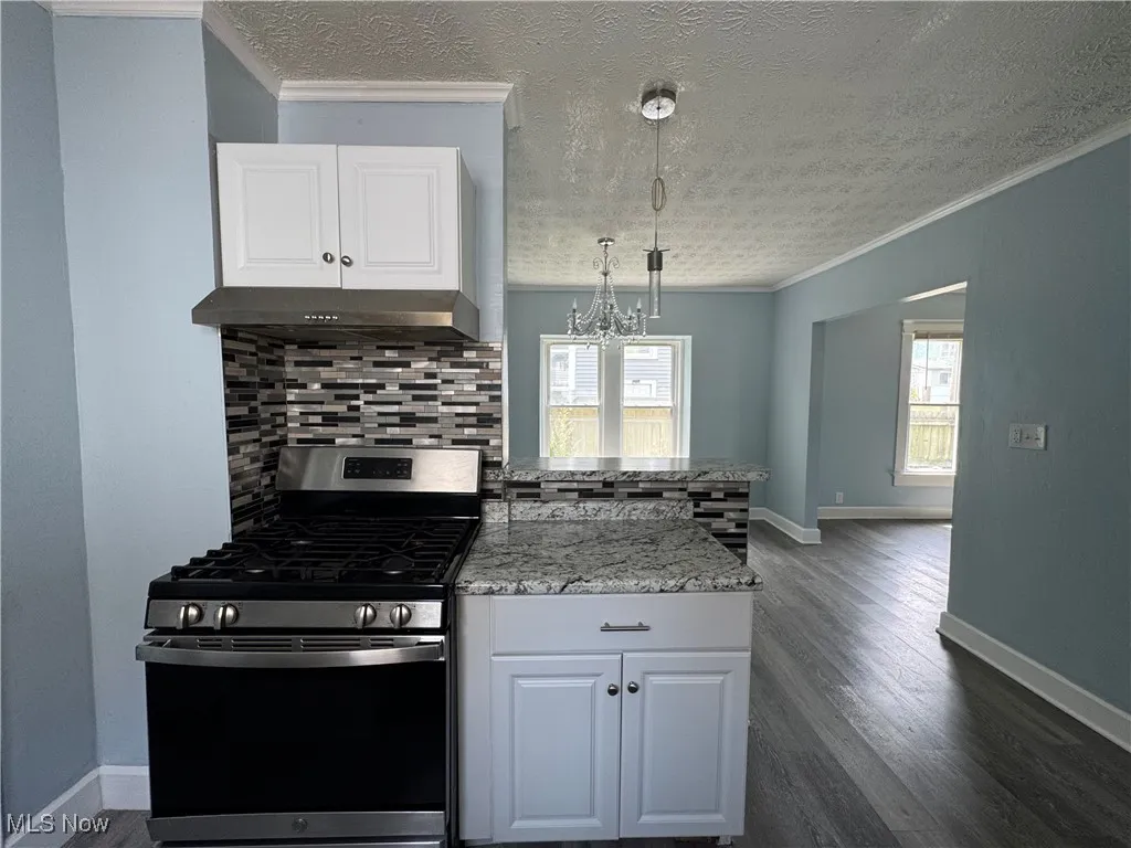 Kitchen featuring stainless steel range with gas stovetop, backsplash, light stone countertops, white cabinets, and crown molding